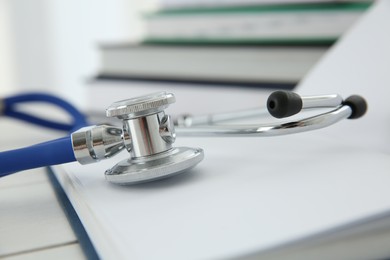 One new medical stethoscope and books on white wooden table, closeup