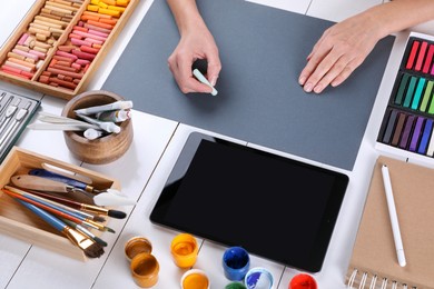 Photo of Artist drawing with chalk pastel on grey paper at white wooden table, closeup