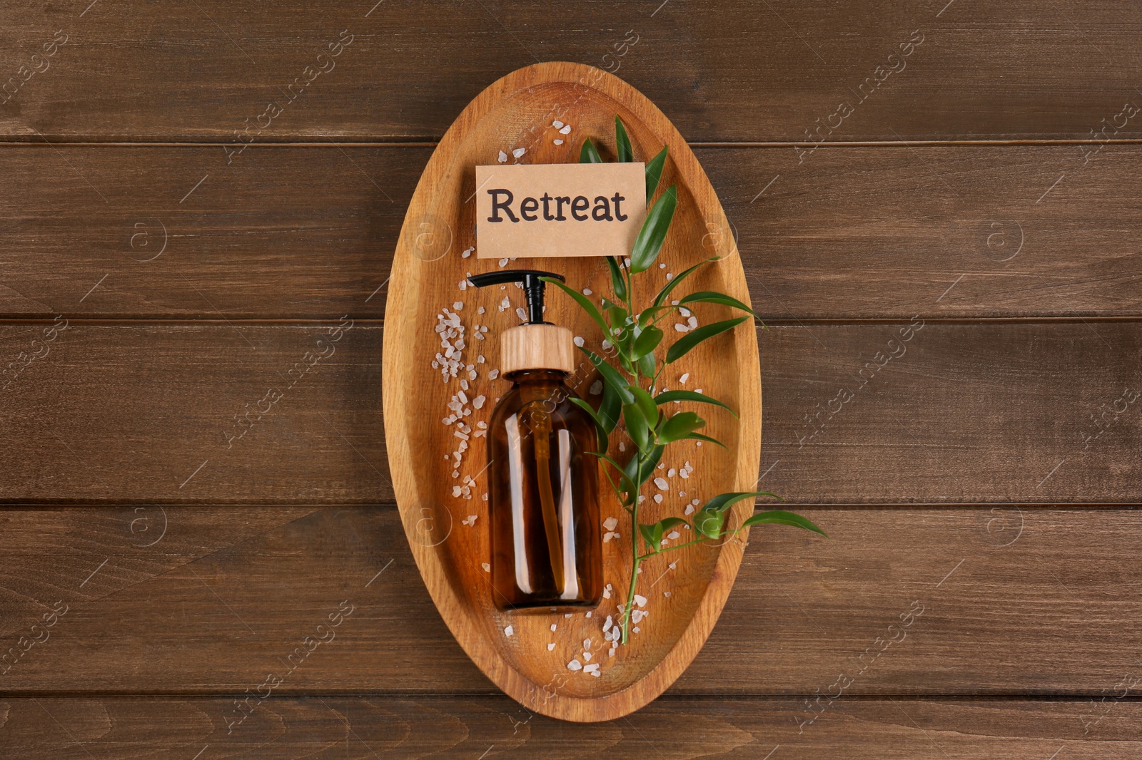 Photo of Card with word Retreat, green branch, cosmetic bottle and sea salt on wooden table, top view