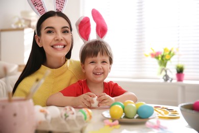 Photo of Happy mother with her cute son painting Easter eggs at table indoors