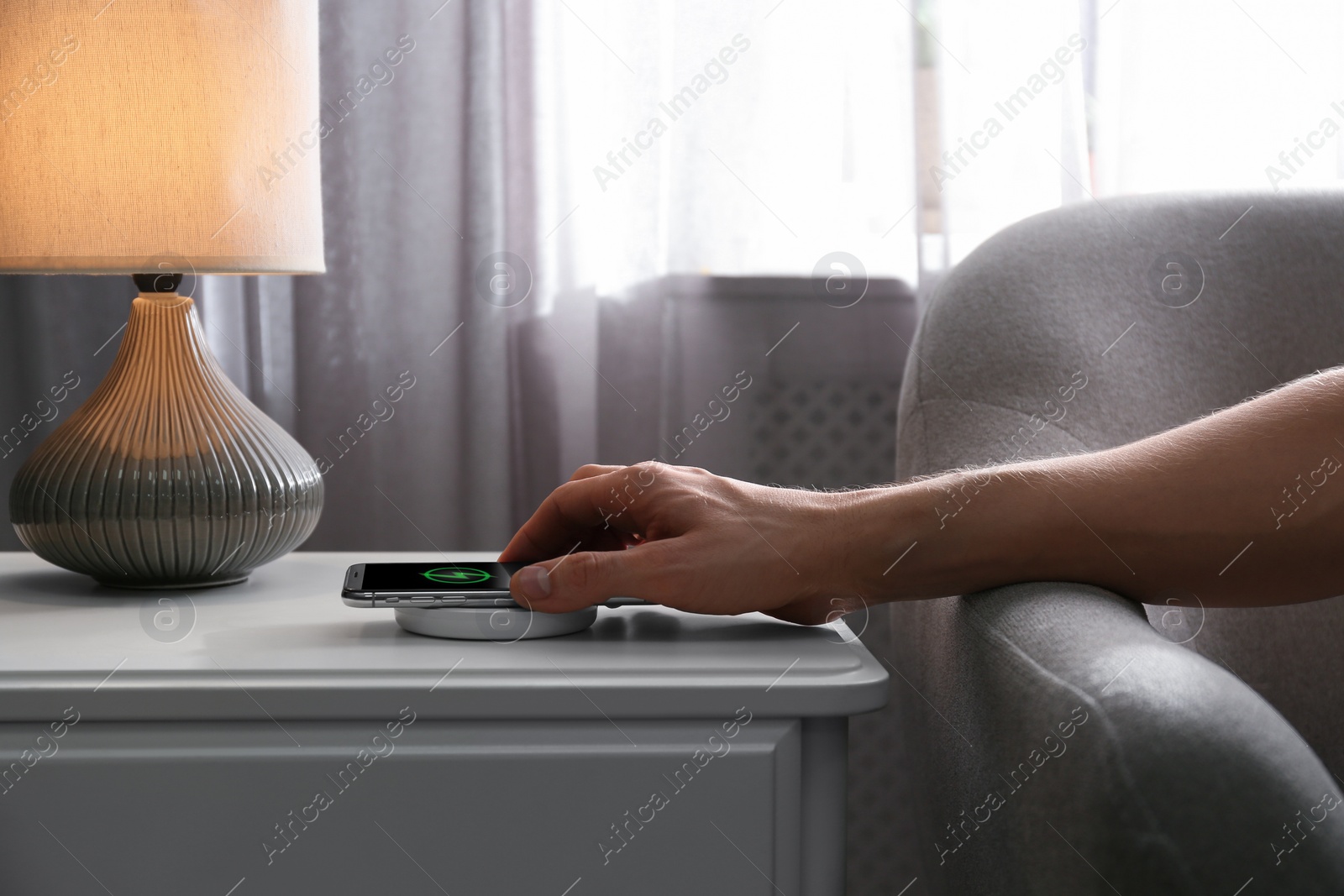 Photo of Man putting smartphone on wireless charger in room, closeup