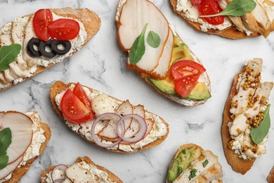 Photo of Different delicious chicken bruschettas on white marble table, flat lay