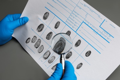 Criminalist studying fingerprints with magnifying glass at table, closeup