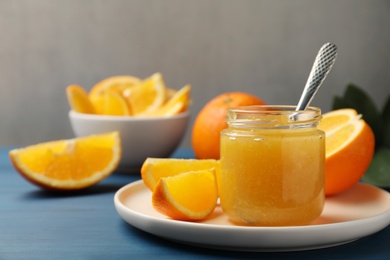 Photo of Delicious orange marmalade and fruit slices on blue wooden table