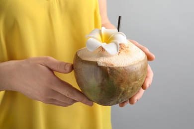 Young woman with fresh coconut cocktail on grey background, closeup