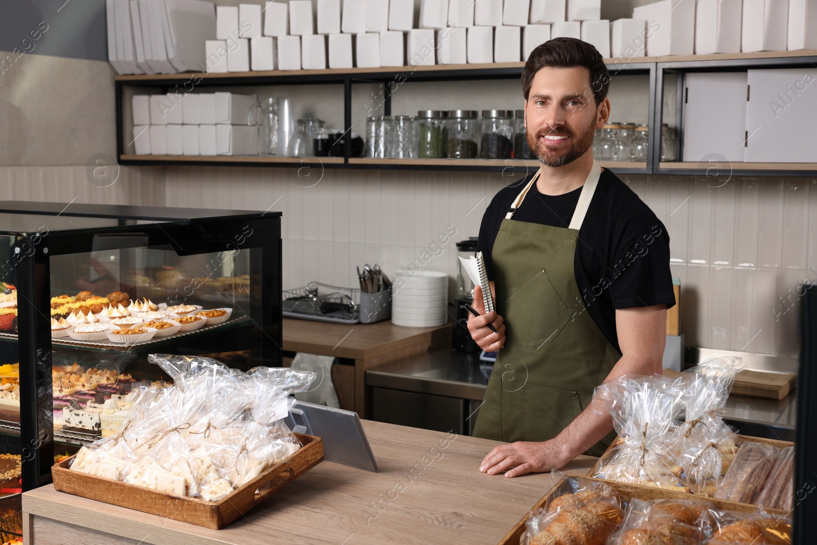 Photo of Happy seller with notebook and pen at cashier desk in bakery shop