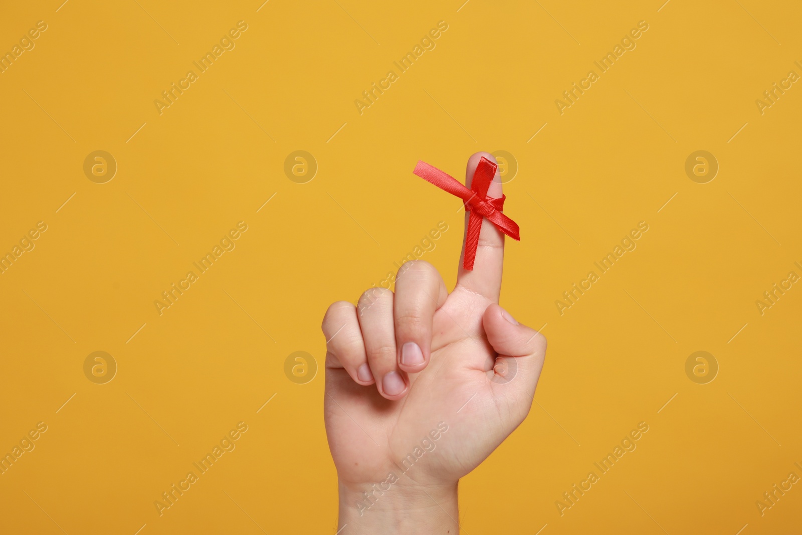 Photo of Man showing index finger with red tied bow as reminder on orange background, closeup