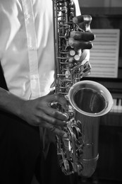 Image of African-American man playing saxophone indoors, closeup. Black and white effect