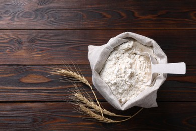 Photo of Sack with flour and wheat spikes on wooden background, flat lay. Space for text