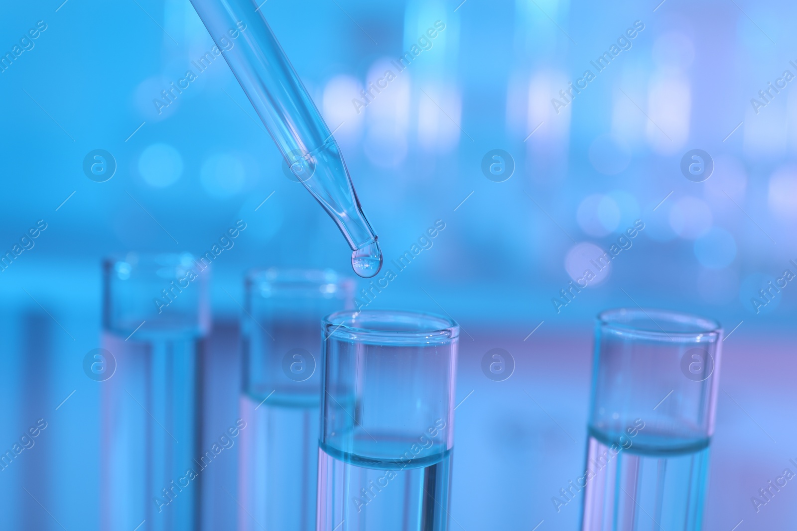 Photo of Dripping liquid from pipette into test tube on light blue background, closeup