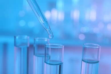 Dripping liquid from pipette into test tube on light blue background, closeup