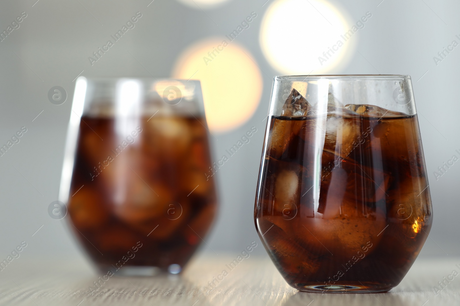 Photo of Glass of cola with ice on table against blurred background. Space for text