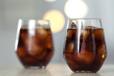 Photo of Glass of cola with ice on table against blurred background. Space for text