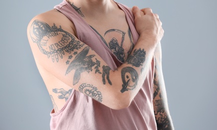 Young man with stylish tattoos on grey background