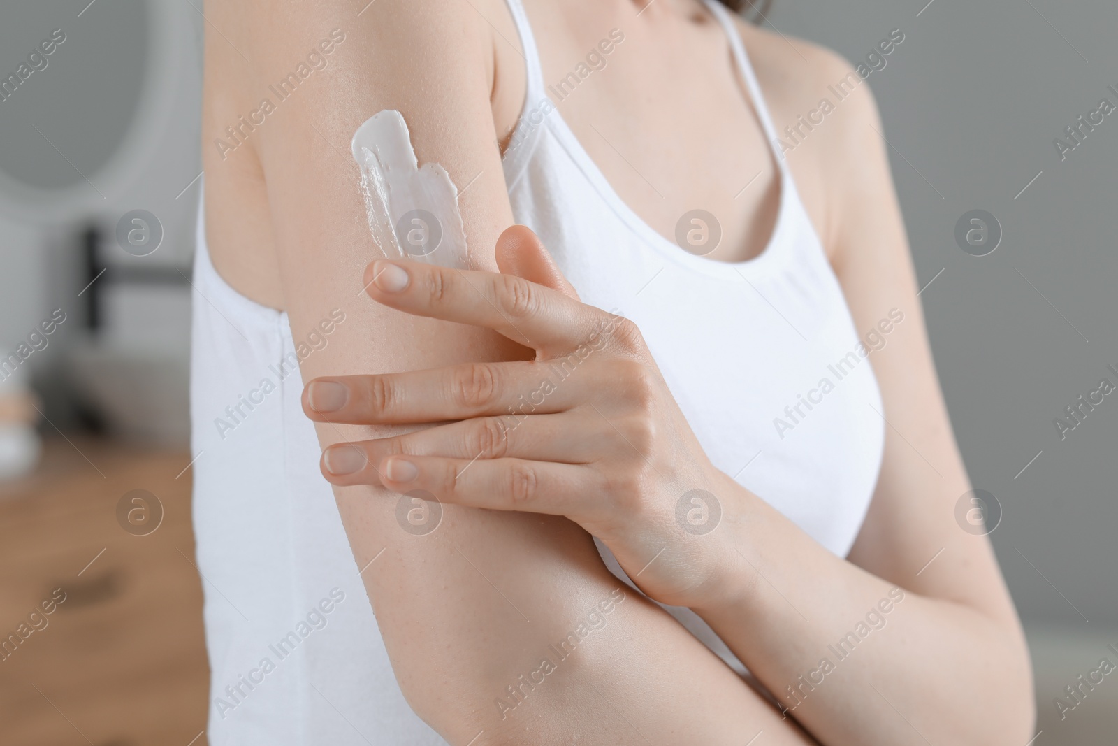 Photo of Woman applying body cream onto arm indoors, closeup