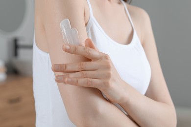 Photo of Woman applying body cream onto arm indoors, closeup
