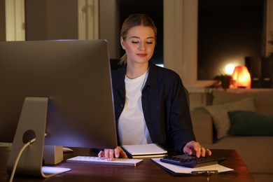 Photo of Home workplace. Woman with calculator near computer at wooden desk in room