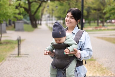 Mother holding her child in sling (baby carrier) in park. Space for text