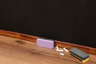 Photo of Pieces of chalk and dusters on wooden table near blackboard, space for text