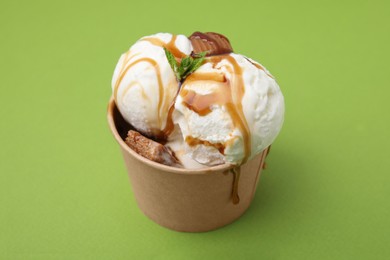 Scoops of tasty ice cream with mint leaves, caramel sauce and candies in paper cup on green background