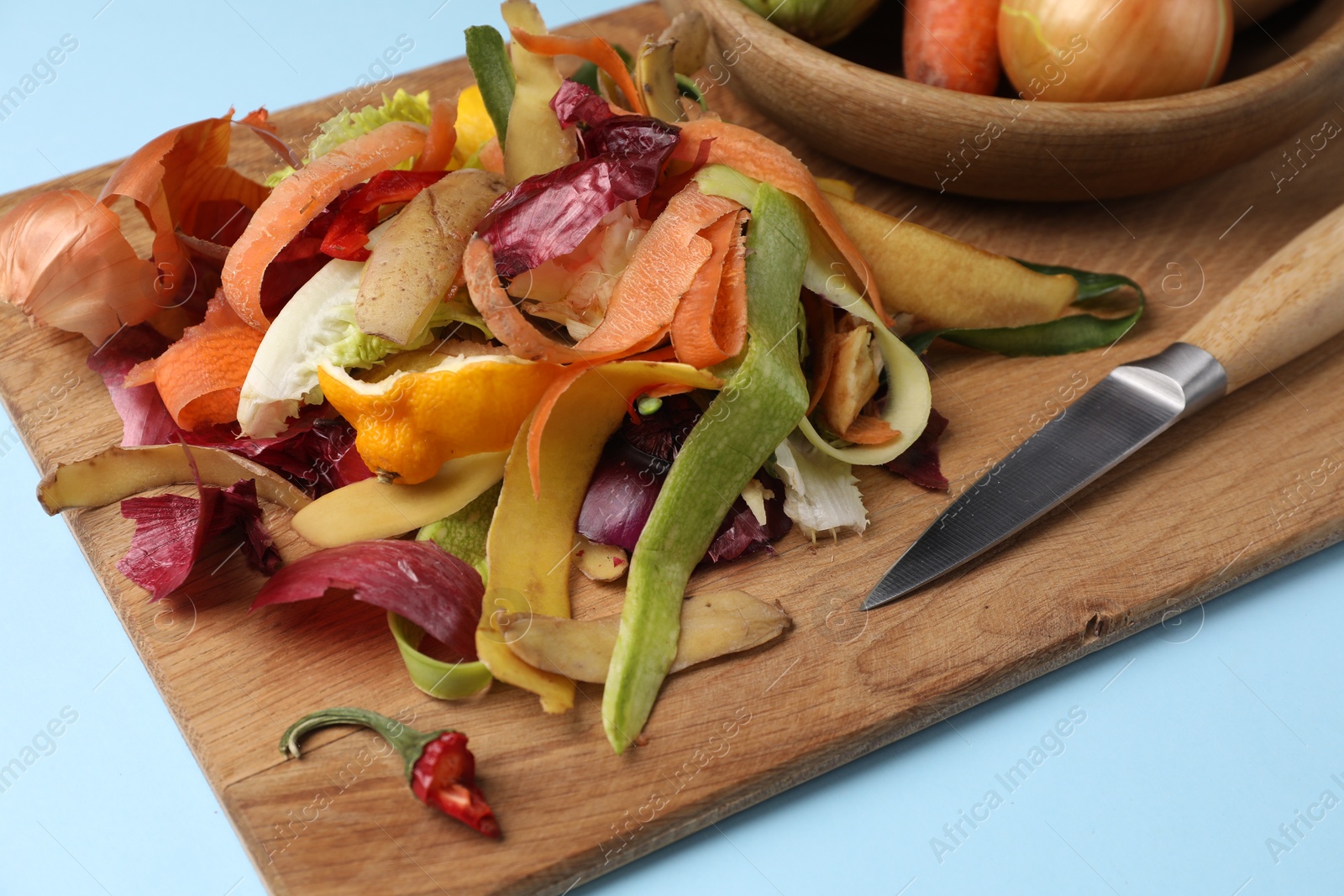 Photo of Different fresh vegetables with peels and knife on light blue background, closeup