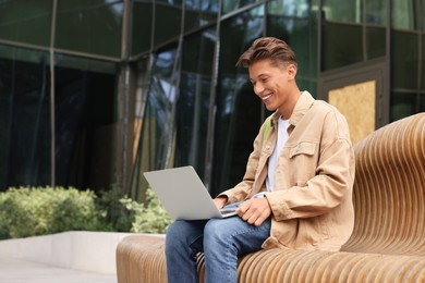 Photo of Happy young student studying with laptop on bench outdoors
