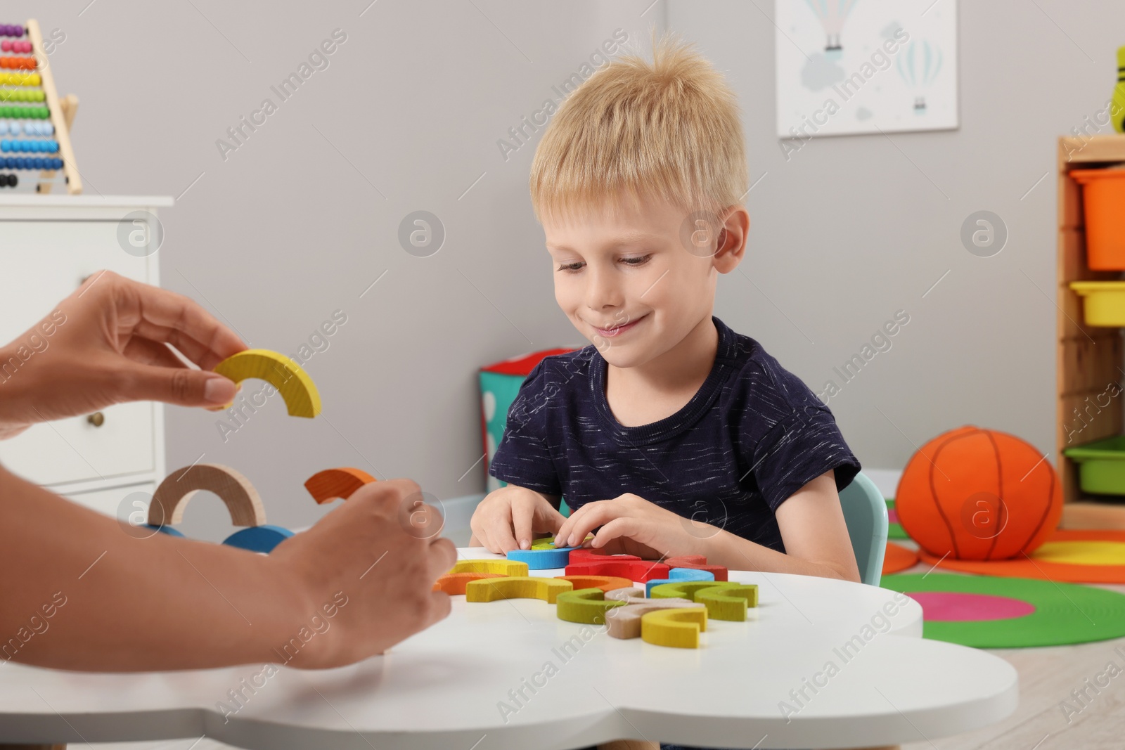 Photo of Motor skills development. Mother helping her son to play with colorful wooden arcs at white table in room