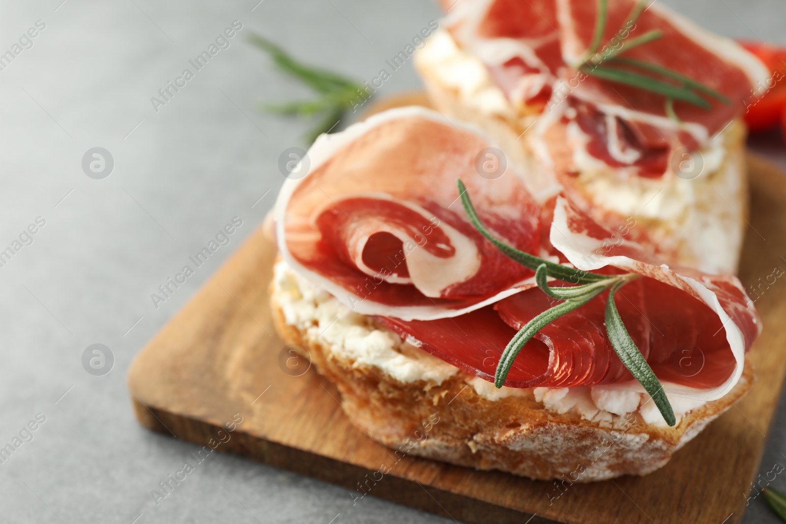 Photo of Tasty sandwiches with cured ham and rosemary on grey table, closeup