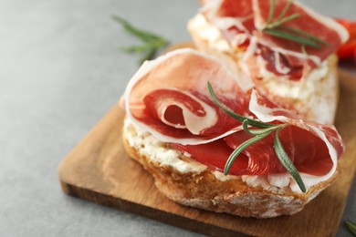 Tasty sandwiches with cured ham and rosemary on grey table, closeup
