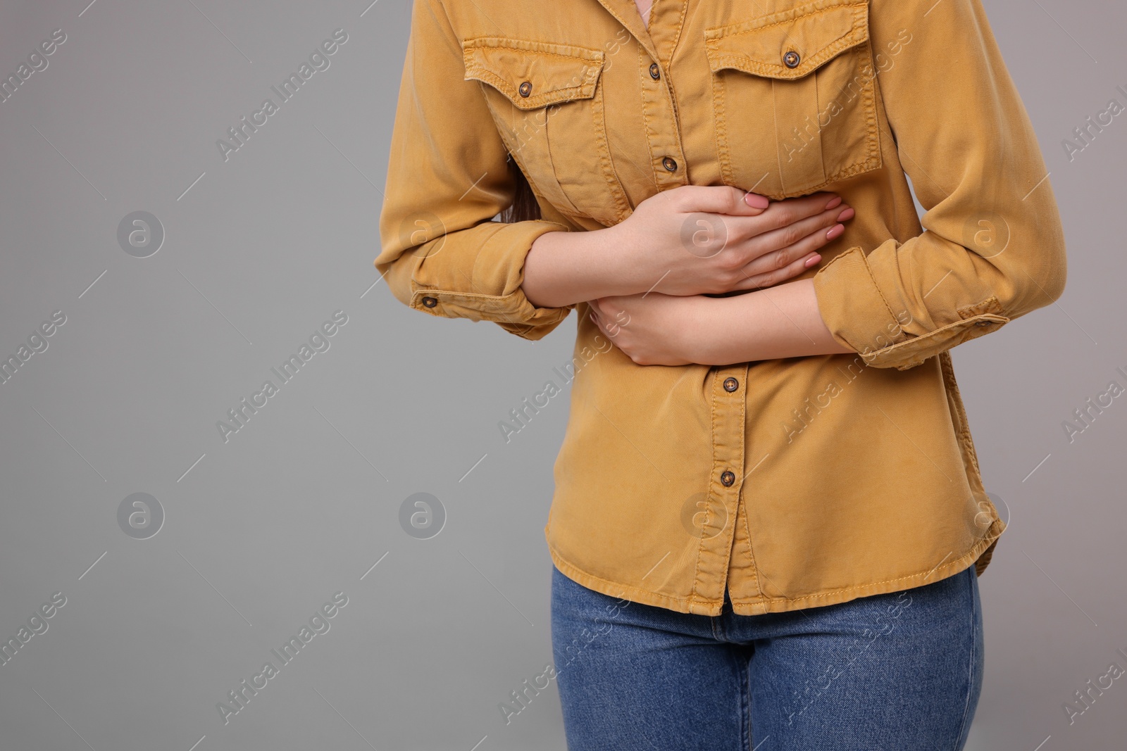 Photo of Young woman suffering from stomach pain on grey background, closeup. Space for text