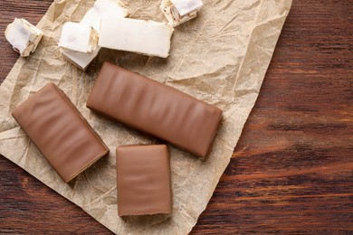 Tasty chocolate bars and nougat on wooden table, top view