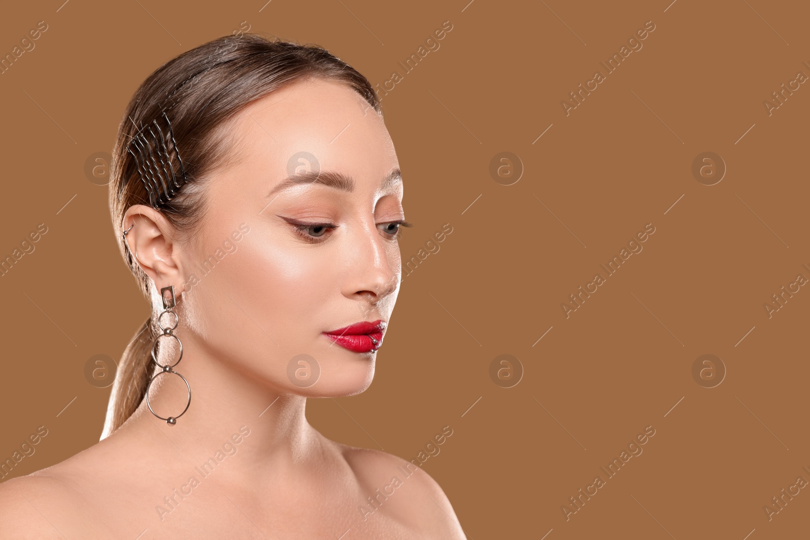 Photo of Young woman with lip and ear piercings on light brown background, space for text