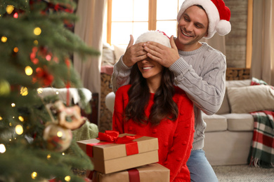 Photo of Happy couple with gift boxes in living room decorated for Christmas