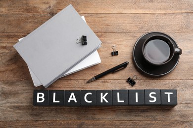 Black cubes with word Blacklist, cup of coffee and office stationery on wooden desk, flat lay