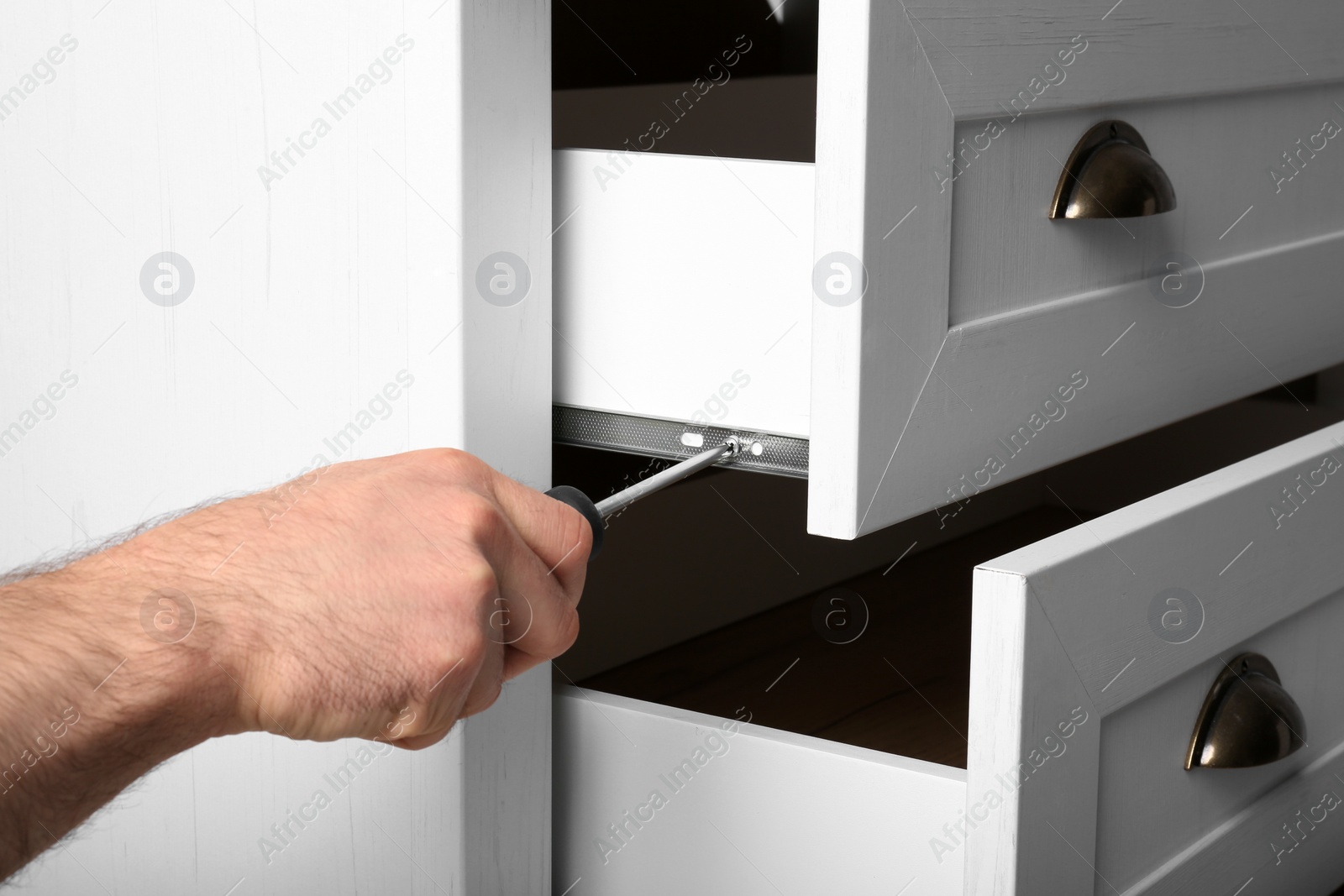 Photo of Man fixing drawer of white wardrobe with screwdriver, closeup