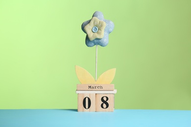 Photo of Decorative toy flower and wooden block calendar on table against color background. International Women's Day