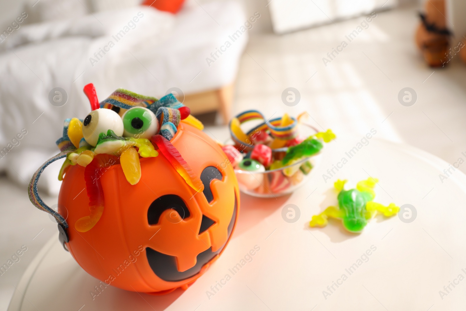 Photo of Halloween trick or treat bucket and many different sweets on white table indoors