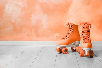 Vintage roller skates on floor near orange wall. Space for text