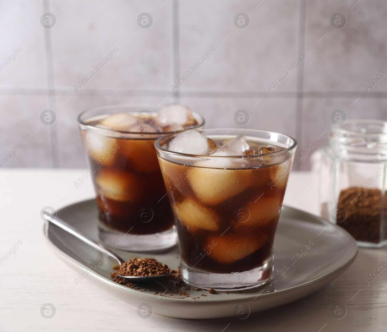 Photo of Refreshing iced coffee with milk in glasses, ingredients and spoon on light table, closeup