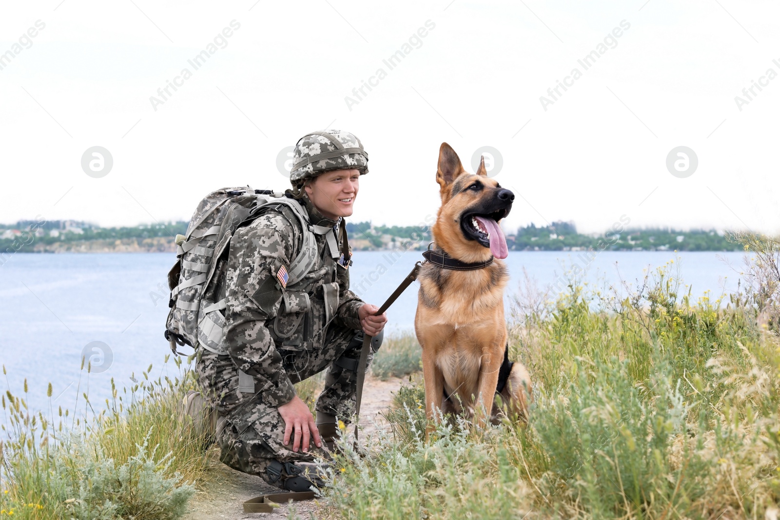 Photo of Man in military uniform with German shepherd dog near river