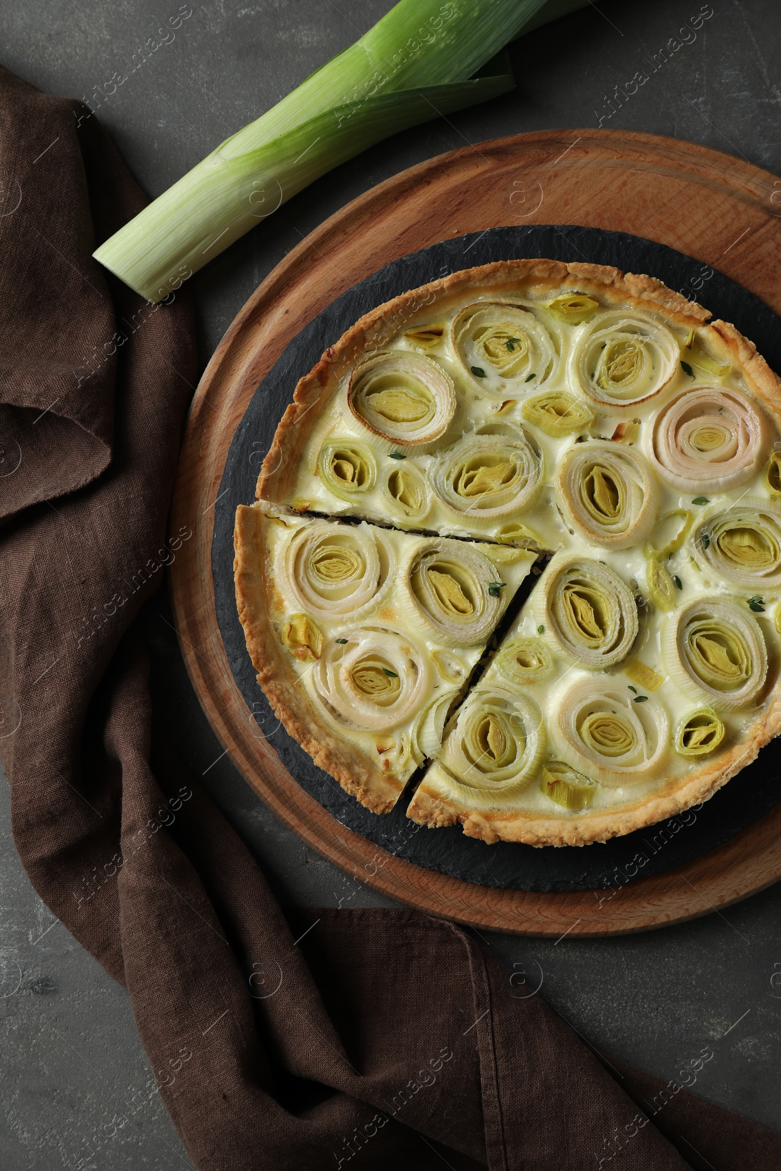 Photo of Tasty leek pie and fresh stalk on dark textured table, flat lay