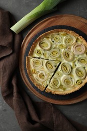 Tasty leek pie and fresh stalk on dark textured table, flat lay