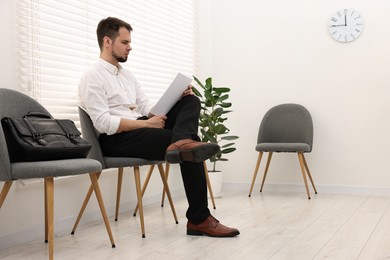 Photo of Man with sheet of paper waiting for job interview indoors