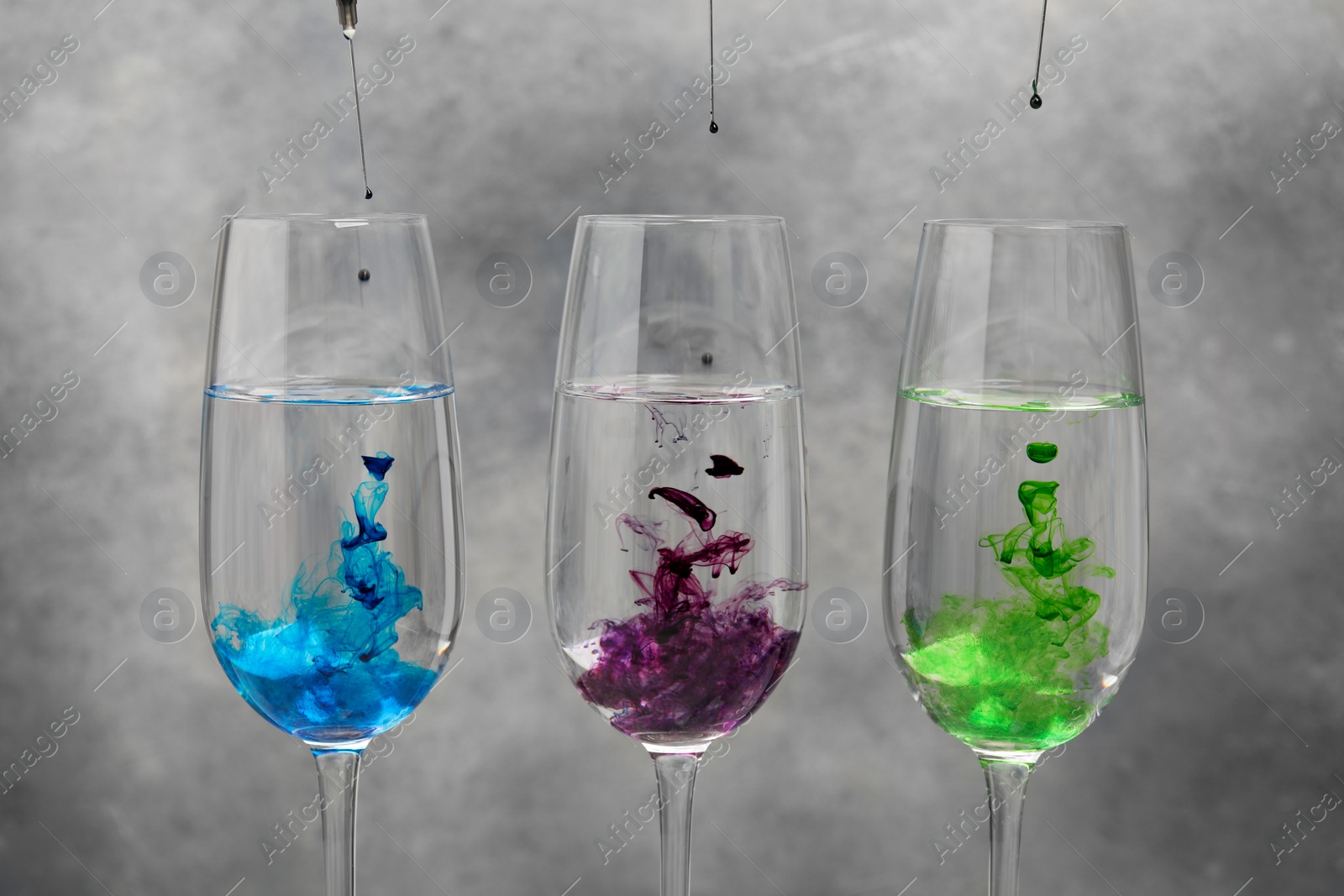 Photo of Different food coloring pouring into glasses on grey background
