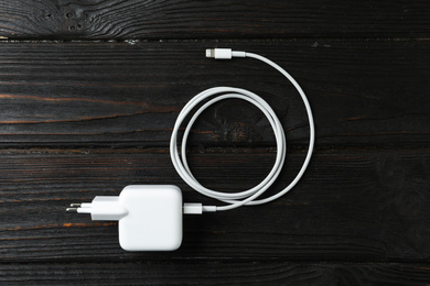 White charging cable and adapter on black wooden table, top view