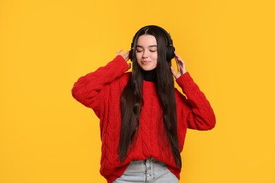 Photo of Teenage girl listening music with headphones on yellow background
