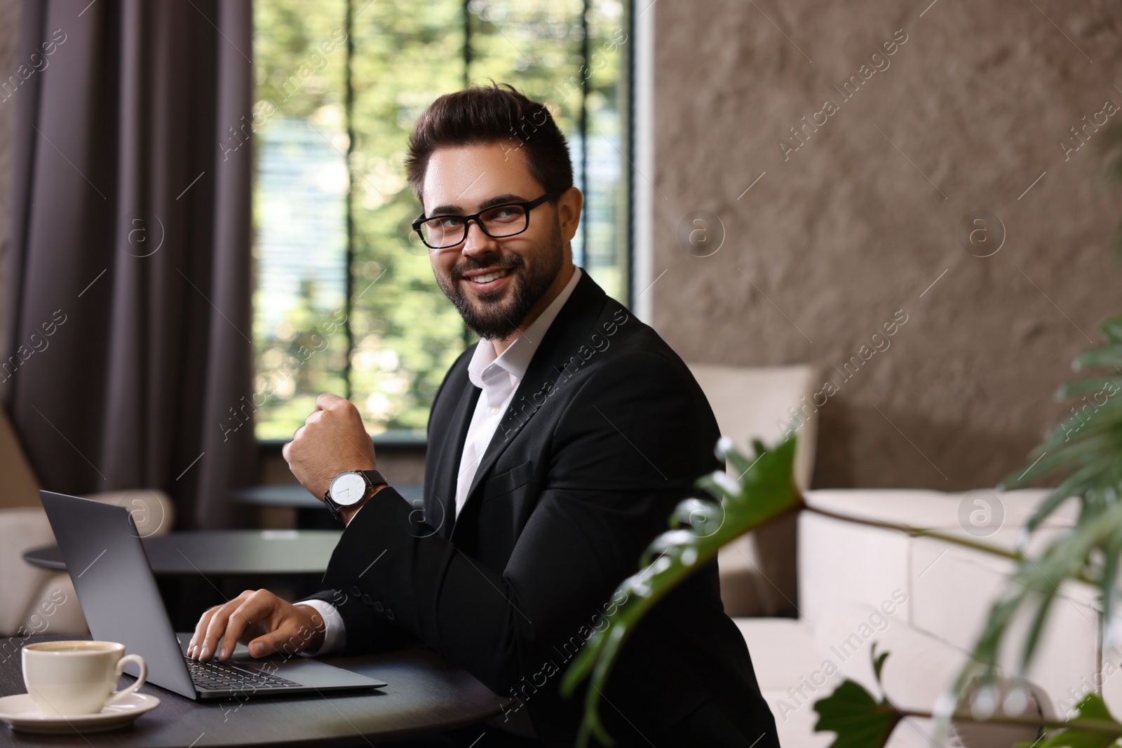 Photo of Happy young man with laptop at table in office