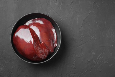 Photo of Pieces of raw beef liver in bowl on black table, top view. Space for text