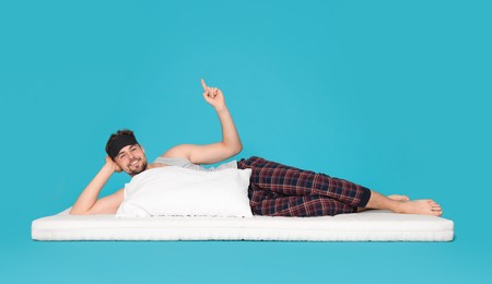 Photo of Man on soft mattress pointing upwards against light blue background