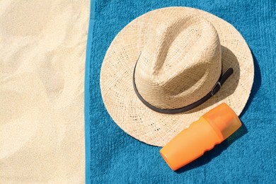 Photo of Soft blue beach towel with straw hat and bottle of sunblock on sand, flat lay